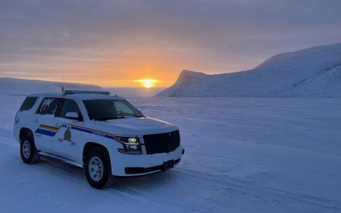 An RCMP police cruiser in the foreground of a snow-covered landscape at sunset.