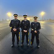 Three RCMP officers stand in uniform under a dusk sky.