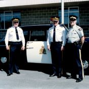 3 men in RCMP uniform post in front of a vintage RCMP patrol vehicle.