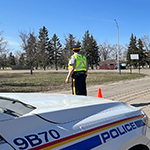 A cadet in a high visibility vest stands on a road in front of a police car.