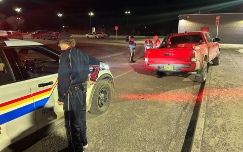 A red truck is pulled over in a parking lot. An RCMP cruiser is behind while multiple uniformed people stand around them.