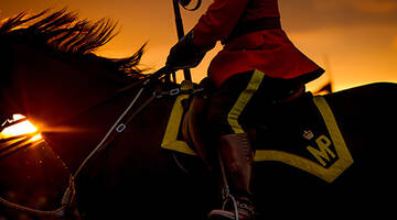 A police officer in red serge rides a black horse as the sun sets behind them