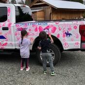 Two children making pink hand prints on an RCMP police truck.