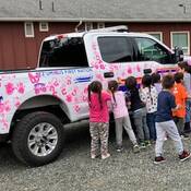 Group of children making hand prints with pink paint on an RCMP truck.