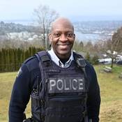 Cst. Dwight Martin stands outside in his uniform smiling with a view of Burrard Inlet in the background