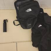 A black canister of bear spray, a black bag and a black jacket on a yellow tile floor.