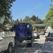 A blue semi-tractor with it’s hood up and several other vehicles parked on either side of the road and a SkyTrain track in the background.