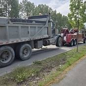 A large dump truck hooked up to a red tow truck on the side of the road.