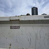 The side of a dump truck with some of the load inside, including some rocks, parked on the side of the road with a high-rise residential building in the background.