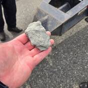 A rock in the hand of a commercial vehicle inspector with the axle of vehicle in the background on a roadway in Burnaby.