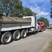 A large dump truck hooked up to a red tow truck on the side of the road.
