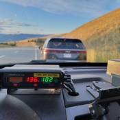 A police radar reads 136 km/h in front of a grey minivan stopped at the side of the highway