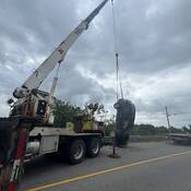 The stolen SUV, seen hanging by its rear axel, is being lowered onto the roadway by a crane. A tow truck is seen in the distance.