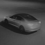 Image of the unknown 4-door sedan, driving through the parking lot with headlights and taillights on;