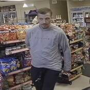 Unknown individual #1, a man with short brown hair, and a goatee. He is seen wearing a grey hoodie with black lettering across the chest and a pair of black pants;