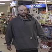 Unknown individual #2, a man with short brown balding hair, and a full beard. He is seen wearing a grey hoodie with a white label on the front pouch;