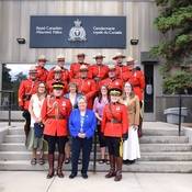 Group photo of some of the M Division medal recipients, some wearing the red serge uniform, standing in four rows, with Commissioner of the Yukon Adeline Webber standing in the middle of the front row.
