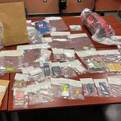 A number of items are displayed on a table, including quantities of drugs, cash, cell phones, tools and drug paraphernalia;