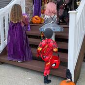 Three children dressed as a witch, alien and superhero walking up stairs while trick-or-treating