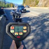 A BC Highway Patrol laser readout that shows 143 km/h while a BMW and its rider are in the background
