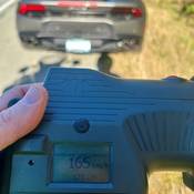A laser reader showing a speed of 165 km/h with a grey Lamborghini in the background