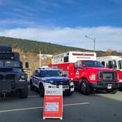 A large RCMP tactical vehicle, a police cruiser, a search and rescue vehicle and a firetruck are lined up next to one another in a parking lot, with a sign for a blood drive laid in front.