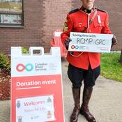 An RCMP NL officer in Red Serge stands next to a sign for a Blood Donation Clinic.