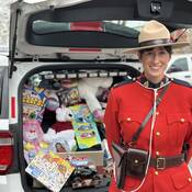 RCMP officer in Red Serge standing in front of a police vehicle filled with toys