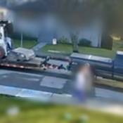 The passenger side of a blue pickup truck towing a flat deck trailer, with a stolen Bobcat loader on it, driving on a side street.