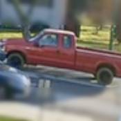 The driver side of a red 2-door pickup truck can be seen driving on a side street.