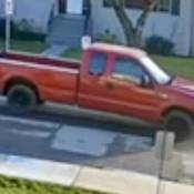 The passenger side of a red 2-door pickup truck can be seen driving on a side street.