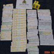 Numerous blurred fraudulent cheques displayed on the floor.