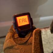 The display of a roadside screening device, being held by someone in brown mittens. The screen reads fail.