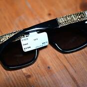 A pair of Chanel sunglasses on a wooden floor with a price tag that states the price is $1,140.