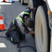 A commercial vehicle inspector inspects a tire on a truck.