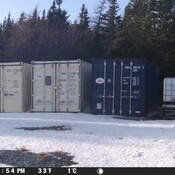 A person walks in front of the same shipping container, during the daylight.