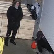 Photo of man wearing black winter coat, black glasses, grey facial hair and woman wearing checkered purple and black jacket and winter boots.