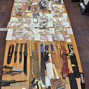 A number of items, including knives, firearms, drugs and drug paraphernalia, are displayed on a table.
