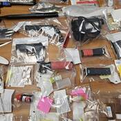 A number of items, including firearms, drugs and drug paraphernalia, are displayed on a table.