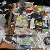 A number of items are displayed in clear evidence bags on a table, including firearms, cash, pills and drugs.