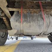 A look under a dump truck shows the fuel tank being secured by two non-rated straps, as the original housing has completely broken off.
