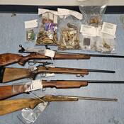 Four bolt action rifles and several evidence bags containing ammunition arranged on a flat surface.