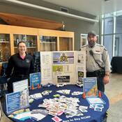 Community services officer and community police officer standing a display table.