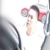 Asian male in his twenties, wearing a white t-shirt looking into a vehicle with a red car in the background.
