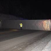 A tractor trailer on its side on Highway #1 with police officers and police vehicles in the background