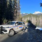 Police vehicle lakeside with mountains in backdrop.