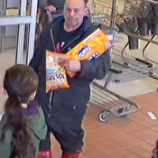 A photo of an unknown male suspect - walking through the entry/exit of a grocery store – while carrying a food item and a case of soda;