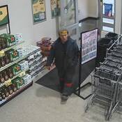 A photo of an unknown male suspect - walking through the entry/exit of a liquor store –  wearing a dark set of coveralls, a toque and sunglasses on his forehead;