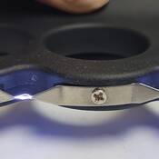 The bottom view of a rechargeable stun gun shaped like a pair of brass knuckles, and is comprised of plastic and metal. The stun gun is activated and arc's of voltage are visible