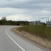 A curved section of the Alaska Highway near Albert Creek in Upper Liard, with a posted maximum speed limit sign of 50 km/h on the roadside.